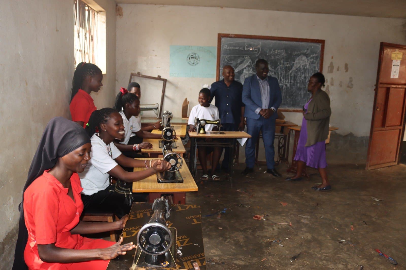 A tailoring class at treadle sewing machines, with visitors observing.