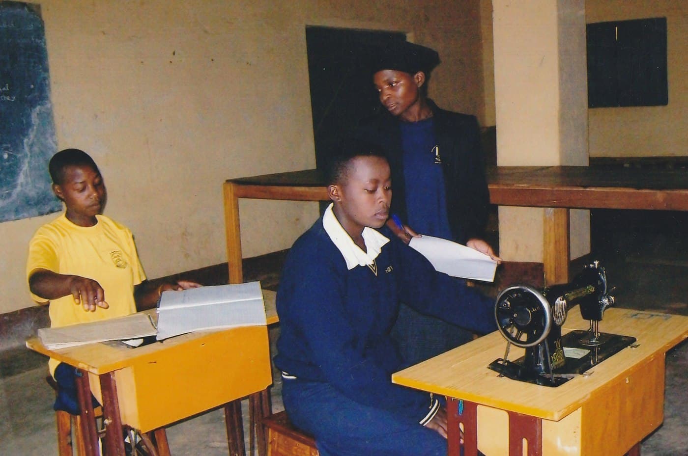 Two students at treadle sewing machines during a tailoring class.